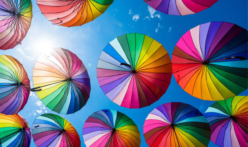 Rainbow umbrellas against a blue sky.